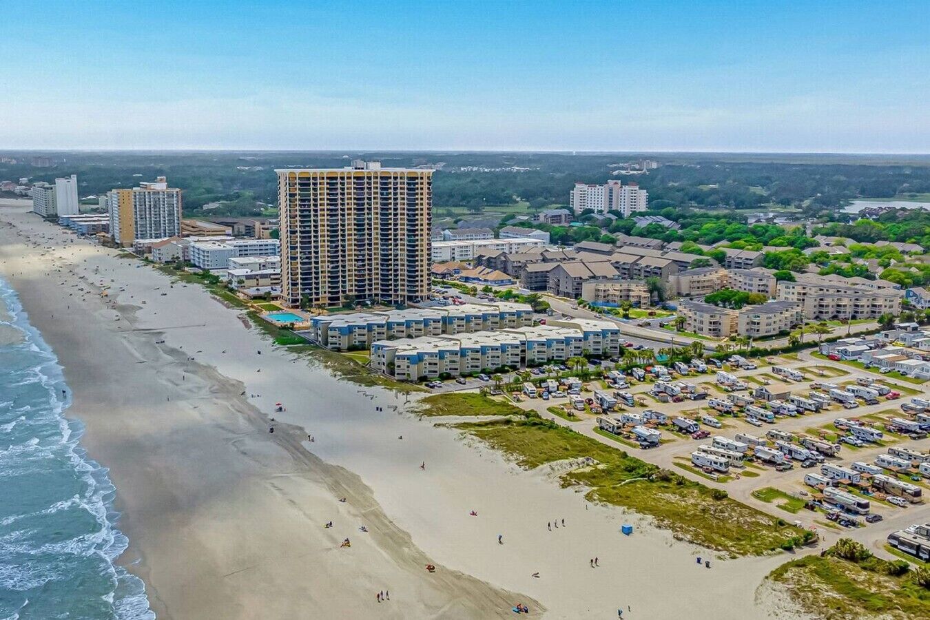 Uma área costeira com um grande hotel, praia e estacionamento para trailers.