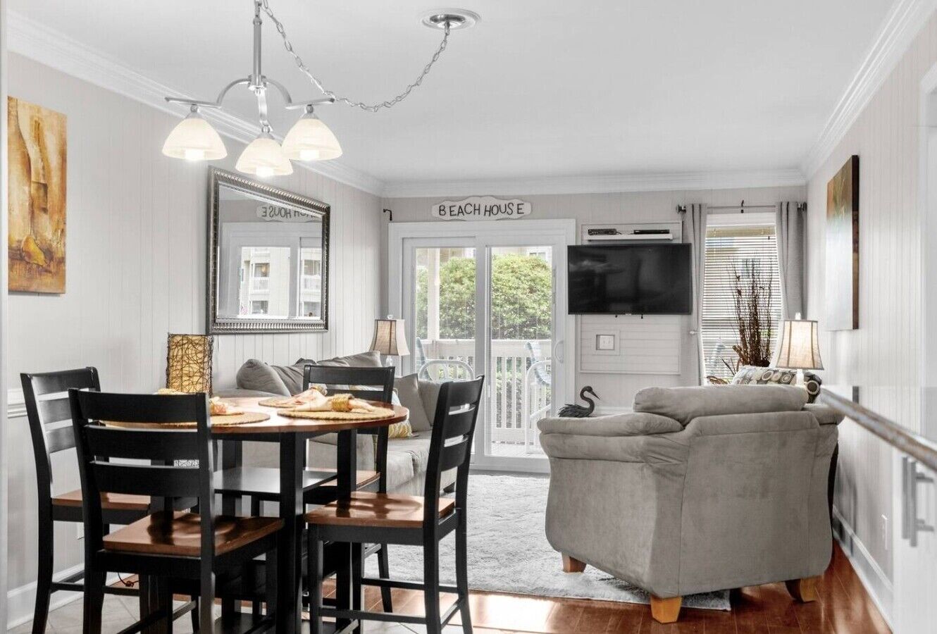 Un comedor con una mesa y sillas, un sofá, un televisor y un cartel que dice 'BEACH HOUSE E'.