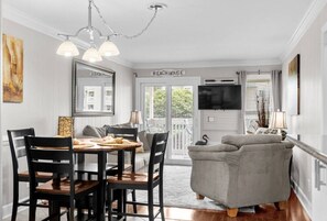 Un comedor con una mesa y sillas, un sofá, un televisor y un cartel que dice 'BEACH HOUSE E'.