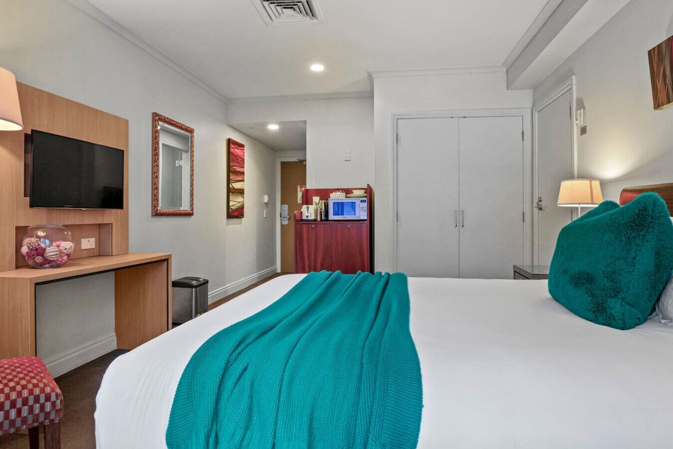 Ett hotellrum med en säng, ett skrivbord, en tv, en garderob och ett badrum.