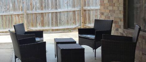 A covered patio area with wicker furniture, a wooden fence, and a brick wall.