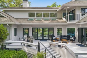 Ein modernes Haus mit Terrasse, Gartenmöbeln und einer Treppe, die zu einem Balkon führt.
