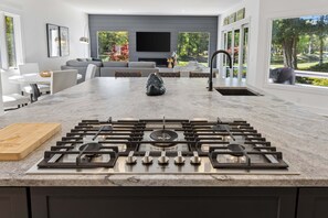 Eine moderne Küche mit einem Gasherd, einer Marmarbeplatte und Blick auf ein Wohnzimmer mit Sofa und Kamin.