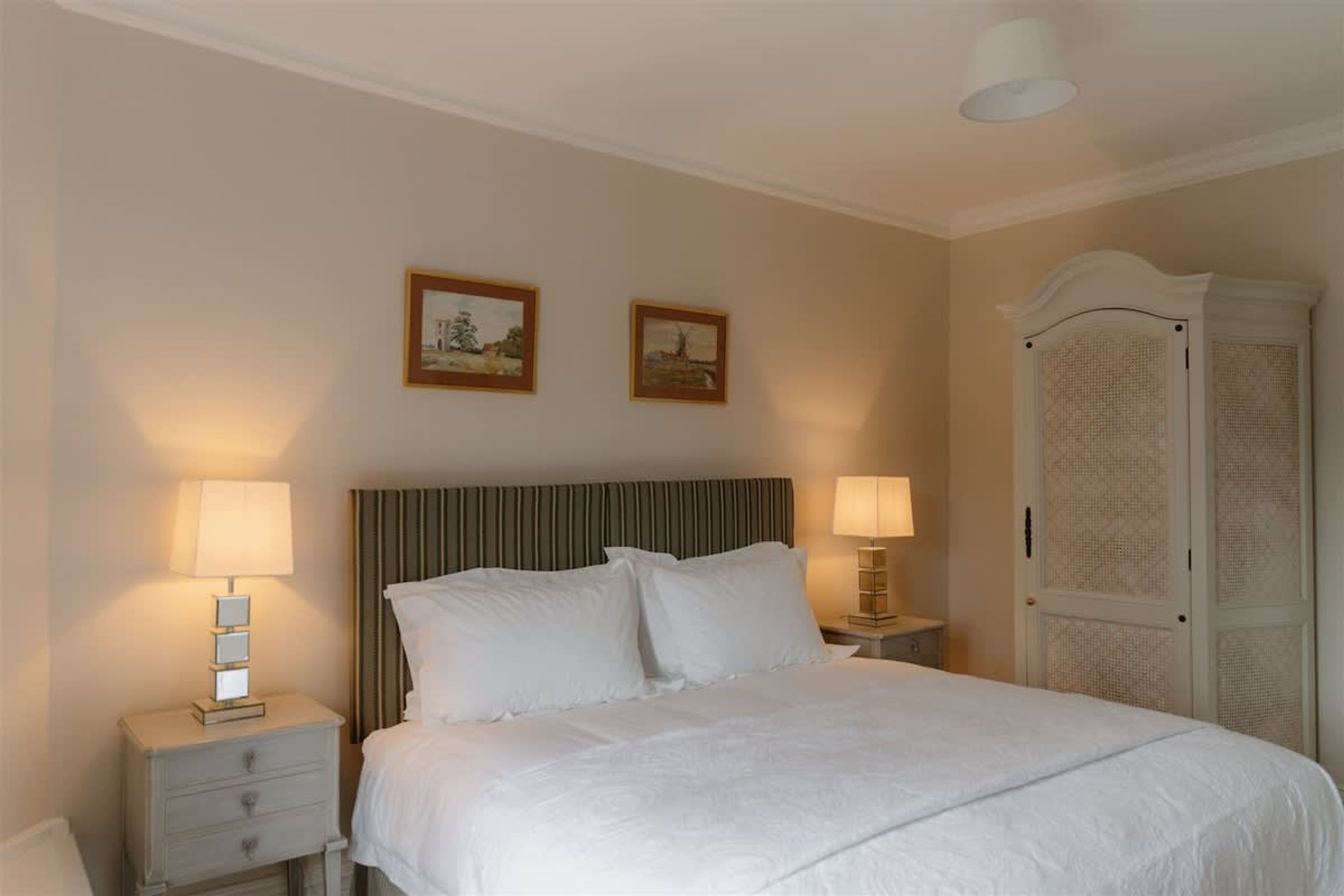 A neatly made bed with two pillows, a bedside table with a lamp, and a wardrobe with a patterned door.
