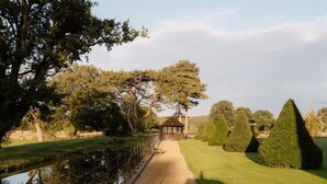 A pathway leading to a gazebo, surrounded by neatly trimmed hedges and trees.