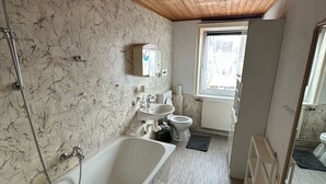 Een badkamer met een houten plafond, een badkuip, toilet, wastafel en een raam.