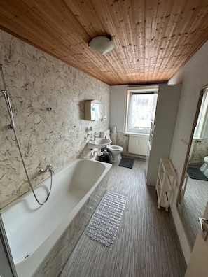 A bathroom with a wooden ceiling, a bathtub, a toilet, a sink, and a window.