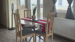 A dining area with a table, chairs, a potted plant, and a window with curtains.