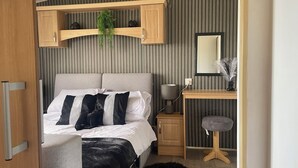 A bedroom with a bed, bedside table, lamp, mirror, and a hanging plant.