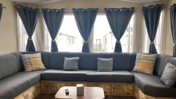 A modern living room with a sectional sofa, a small wooden coffee table, and a view through large windows with curtains.