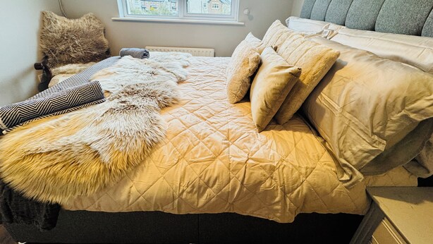 Ein Schlafzimmer mit Bett, Kissen, einem Fellüberwurf, einem Fenster und Blick auf Häuser.