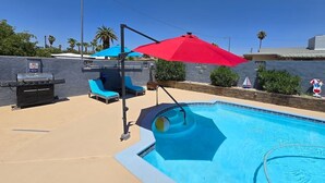 A swimming pool with a red umbrella, lounge chairs, and a barbecue grill. - Private Studio - 10 minutes from LV Strip, airport, and Convention Center (Las Vegas)