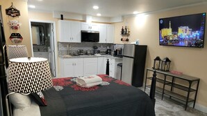 A compact hotel room with a bed, a small kitchenette, a dining area, and a TV displaying a cityscape. - Private Studio - 10 minutes from LV Strip, airport, and Convention Center (Las Vegas)