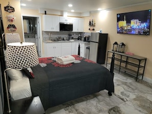 A compact hotel room with a bed, a small kitchenette, a dining area, and a TV displaying a cityscape. - Private Studio - 10 minutes from LV Strip, airport, and Convention Center (Las Vegas)
