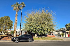 A residential street with a black car parked on the side, a large tree, and houses in the background. - Private Studio - 10 minutes from LV Strip, airport, and Convention Center (Las Vegas)