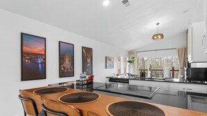 A modern kitchen with a central island, white cabinetry, and a dining area with a wooden table and chairs. - Game Room Condo Walk to The Landing with Pools and Creek Views, Family Friendly (Branson)