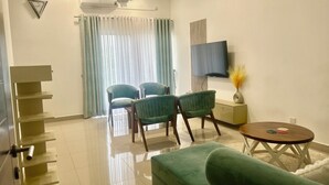 A modern living room with a flat-screen TV, two green armchairs, a green sofa, a small wooden table, and a ceiling fan. -  Cozy 3BR Condo with AC at Negombo Santorini Resort, Close to Airport (Negombo)