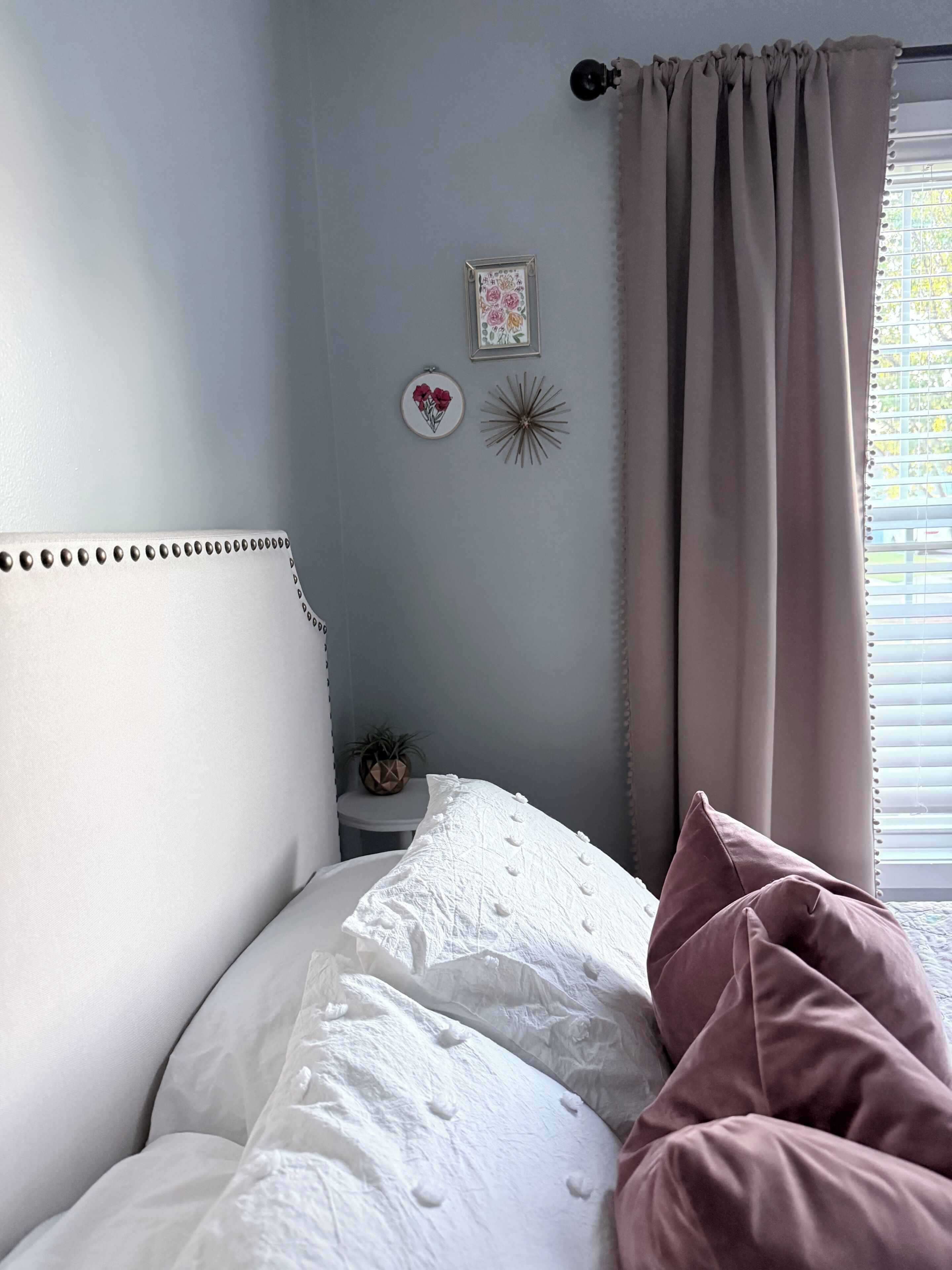 A bedroom with a bed, a nightstand, a framed picture, and a window with curtains.