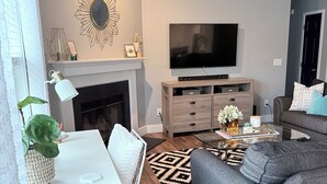 Ein modernes Wohnzimmer mit Kamin, Flachbildfernseher, einer Couch, einem Couchtisch und einem gemusterten Teppich.