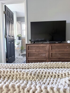 A room with a bed, a television on a wooden dresser, and a door leading to another room. - Stylish 3-bedroom house, 15 minutes from the beach! (Wilmington)