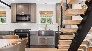 A modern kitchen with dark cabinets, a microwave, an oven, and a sink. There is a dining table with chairs and a staircase with wooden steps. - Charming Inlet Beach Compound | Pool + Walk to Rosemary Beach (Inlet Beach)
