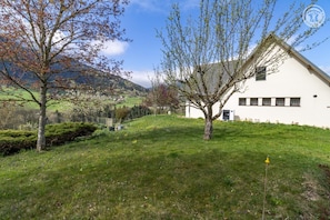 A white building with a sloped roof, surrounded by a grassy area with trees and a mountain in the background. - La Posette - LE CHATELARD (LE CHATELARD)