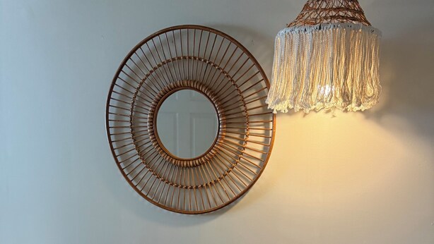 Un espejo circular fijado a la pared, una consola de madera con cajones y un colgador de luz.