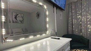 A room with a vanity mirror, a television mounted on the wall, a leopard print pillow, and a green chair. - 2BR.KingBed.NearStadiums.BalconyAccess.NoStairs (Arlington)