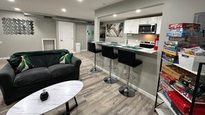 A modern kitchen with white cabinets, a microwave, and a gas stove. There are two black bar stools and a white table with a marble top. - 2BR.KingBed.NearStadiums.BalconyAccess.NoStairs (Arlington)