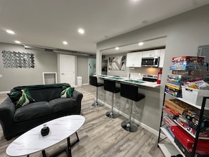 Uma cozinha moderna com armários brancos, micro-ondas e fogão a gás. Há dois bancos pretos e uma mesa branca com tampo de mármore.