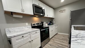A modern kitchen with white cabinets, a stainless steel refrigerator, a microwave, and an oven. - 2BR.KingBed.NearStadiums.BalconyAccess.NoStairs (Arlington)