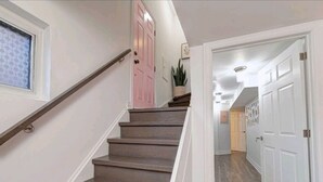Un escalier avec des marches en bois et des murs blancs, menant à une pièce dotée d’une porte et d’une plante.