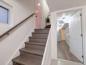 A staircase with wooden steps and white walls, leading to a room with a door and a plant.