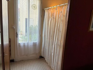 Une pièce dotée d’un sol carrelé, d’une porte ornée d’un rideau en dentelle et d’une fenêtre avec un rideau à motifs.