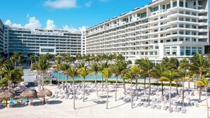 A resort with multiple hotel buildings, a pool area, and a beach with sun loungers and palm trees.