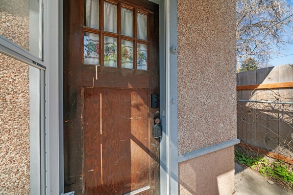 A wooden door with a window above it, a keypad lock, and a textured wall.