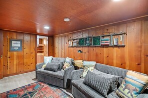 A cozy room with wooden walls, a sofa set, a rug, and a shelf with books and decorative items. - The  Yellowbike  Den (Livingston)
