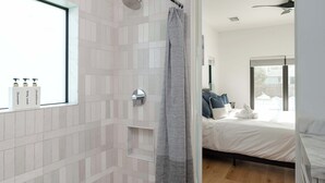 A modern bathroom with a shower, a window, and toiletries on the wall.
