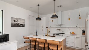 A modern kitchen with a central island, pendant lights, and a dining area with bar stools.
