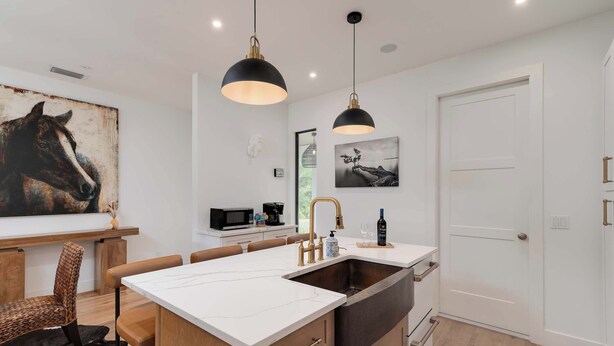 A modern kitchen with a large island, pendant lights, and a dining area with chairs.