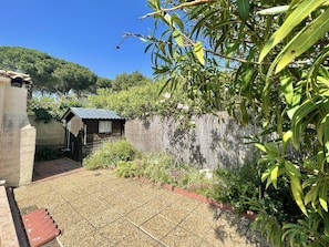 A garden with a small wooden structure, a stone wall, and a tiled patio area. - CAP D'ADGDE - La Pinède / Réf 141 (CAP D'AGDE)