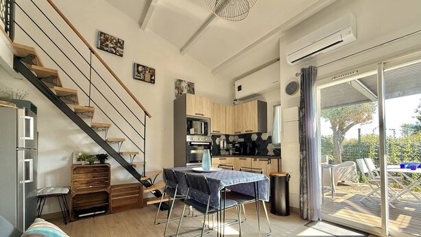 Una cucina moderna con mobili in legno, un'area pranzo con tavolo e sedie, una scala e una porta scorrevole in vetro che dà su un patio esterno.