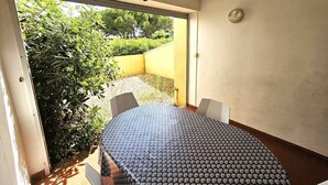 A room with a round table, two chairs, a sliding glass door leading to a garden, and a wall-mounted light fixture. - CAP D'AGDE - Plage du Môle / Réf 230 (CAP D'AGDE)