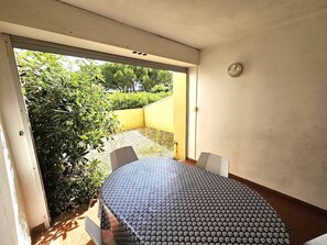 A room with a round table, two chairs, a sliding glass door leading to a garden, and a wall-mounted light fixture. - CAP D'AGDE - Plage du Môle / Réf 230 (CAP D'AGDE)