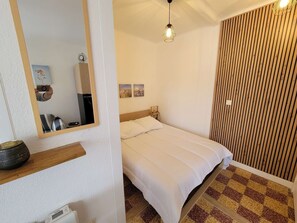 Un dormitorio con cama, espejo, estante con un objeto decorativo, lámpara de pared y panel de pared texturizado.