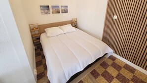 A neatly made bed with white bedding, a wooden headboard, and a checkered floor pattern. - Lovely studio fo 2 or 3 people, only 100m away from the beach of Portiragnes plage (PORTIRAGNES)