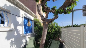 A small outdoor area with a tree, two chairs, a window with curtains, and a white wall. - Lovely studio fo 2 or 3 people, only 100m away from the beach of Portiragnes plage (PORTIRAGNES)