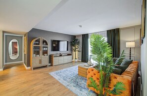 A modern living room with a wooden cabinet, a flat-screen TV, a sofa, and a large plant.