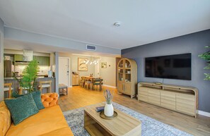 A modern living room with a sofa, a dining area, a kitchen, and a TV mounted on the wall.