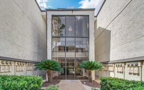 Un edificio con entrada de vidrio, dos plantas en macetas y buzones en el suelo.